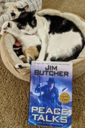 A cat and kitten curled up sleeping with a copy of the book Peace Talks by Jim Butcher in the foreground