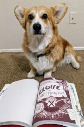 In the foreground a book open to "Eloise at Christmastime" behind it a sitting corgi dog.