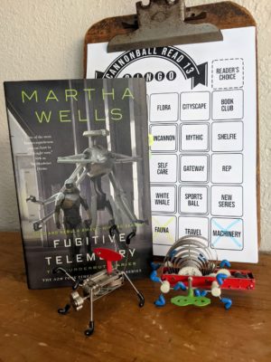 The book Fugitive Telemetry is standing next to two wind up robot toys.
