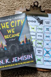 The book The City We Became by N.K. Jemisin lying on top of a clipboard holding a book bingo sheet