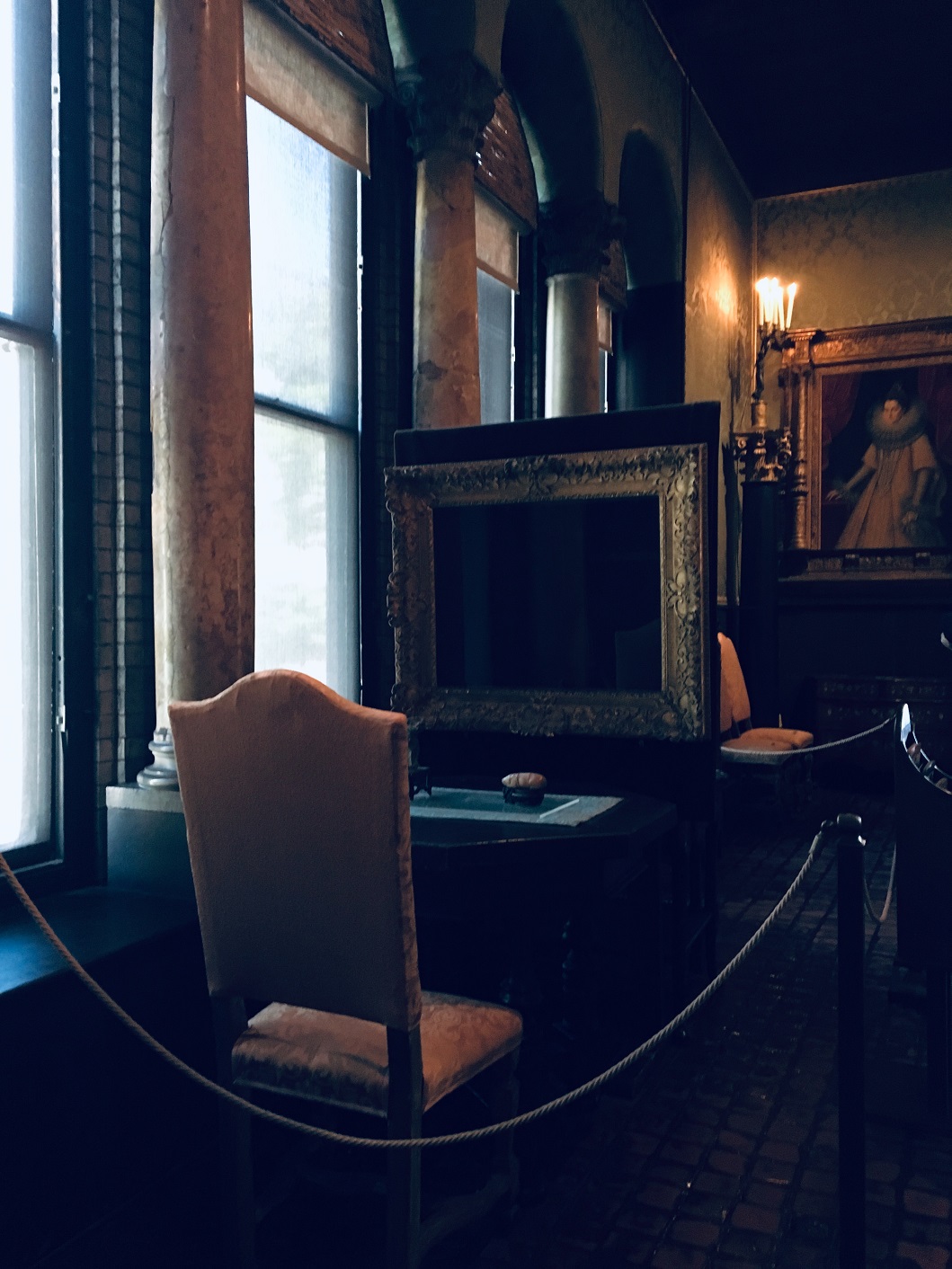 Dark Photograph of an empty chair pointed at a desk, above which sits an empty frame