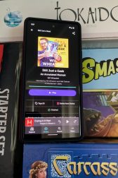 A cell phone showing an audiobook of "Still Just a Geek: An Annotated Memoir" by Wil Wheaton surrounded by board games.