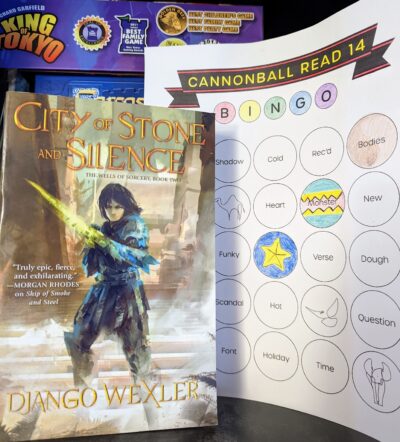 The book, "City of Stone and Silence" by Django Wexler standing next to a book bingo card.