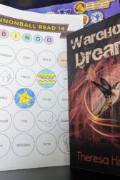 The book "Warehouse Dreams" by Theresa Halverson standing next to a book bingo card.