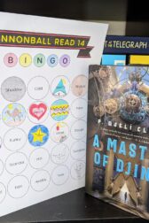 The book,"A Master of Djinn" by P. Djeli Clark, standing next to a book bingo card