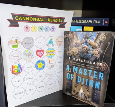 The book,"A Master of Djinn" by P. Djeli Clark, standing next to a book bingo card