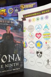 The book, "Nona the Ninth" by Tamsyn Muir standing next to a mostly filled out book bingo card.