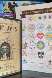 The book, "The Golden Enclaves" by Naomi Novik standing next to a book bingo card mostly filled out.