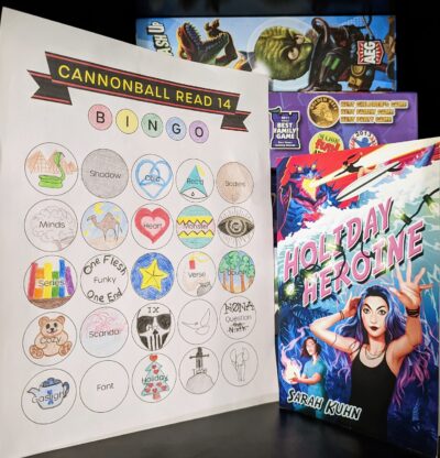 The book "Holiday Heroine" by Sarah Kuhn standing next to a mostly full book bingo card.
