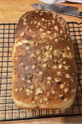 A loaf of Toasting Bread on a cooling rack. The loaf is topped with oat flakes.