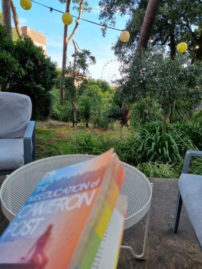 the book of The Miseducation of Cameron Post being read at an outdoor cafe on a clear summer evening