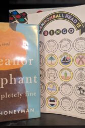 The book, "Eleanor Oliphant is Completely Fine", by Gail Honeyman, is standing next to a partially complete book bingo card.