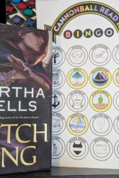 The book, "Witch King" by Martha Wells standing next to a partially completed book bingo card.