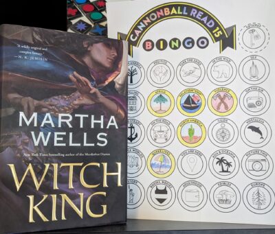 The book, "Witch King" by Martha Wells standing next to a partially completed book bingo card.