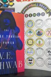 The book, "The Fragile Threads of Power" by V.E. Schwab standing next to a partially complete bingo card.