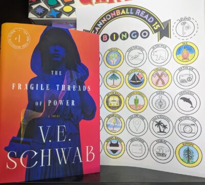 The book, "The Fragile Threads of Power" by V.E. Schwab standing next to a partially complete bingo card.