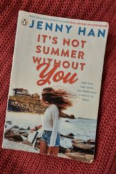 It's Not Summer Without You Cover. A girl on a beach in short denim shorts, with long hair, looking back towards a big beach house.