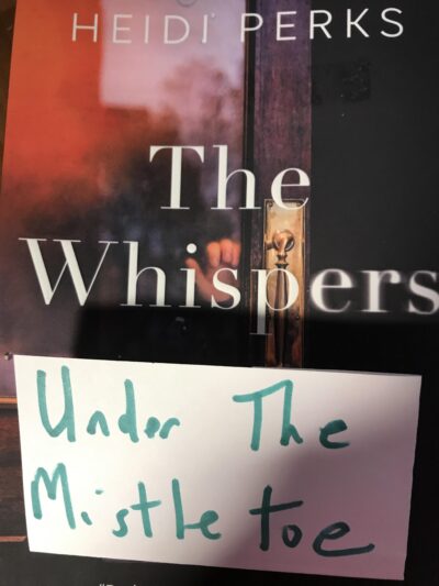 A cover of Heidi Perks’ The Whispers, with a piece of paper under the title with “under the mistletoe” written on it.