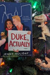The book, "Duke, Actually" held in front of a Christmas tree.