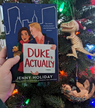 The book, "Duke, Actually" held in front of a Christmas tree.