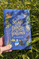 The book, "The Secret Lives of Country Gentlemen" held in front of a stand of bamboo.