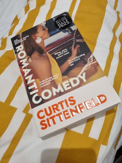 Cover of Romantic Comedy--a woman in a yellow halter top and sunglasses driving a car