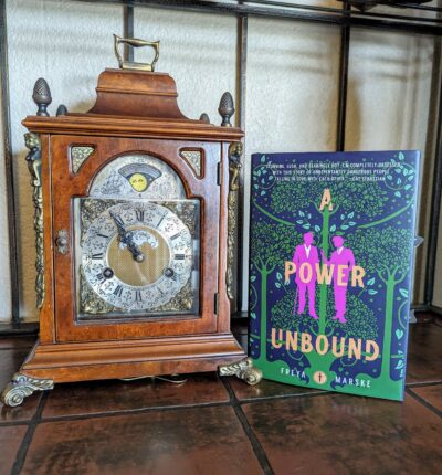 The book, "A Power Unbound" by Freya Marske, standing next to a small ornate clock.