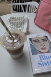 Copy of Blue Sisters, which has the painted face of a woman, on a table with an iced coffee